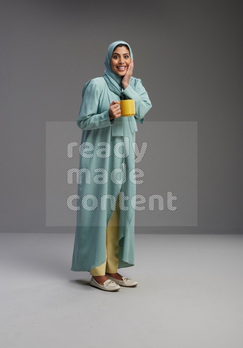 Saudi Woman wearing Abaya standing  holding a mug on Gray background