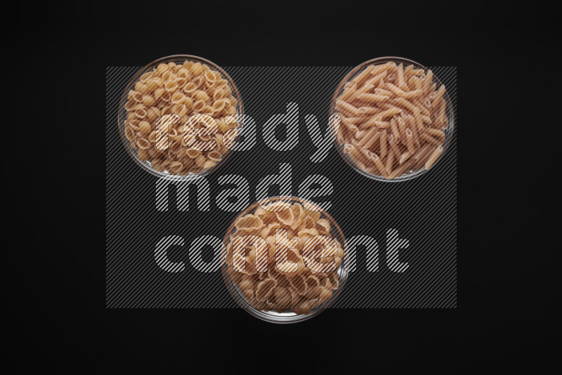 Different pasta types in glass bowls on black background