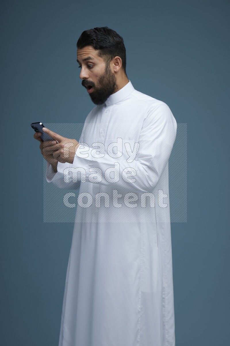 A man Texting in a blue background wearing Saudi Thob