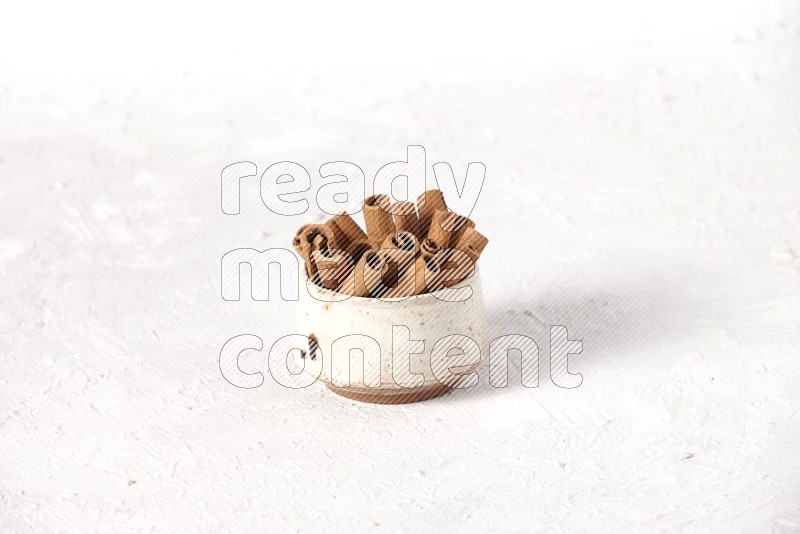 Cinnamon sticks in a beige bowl on a white background