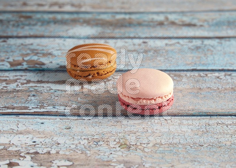 45º Shot of of two assorted Brown Irish Cream, and Pink Litchi Raspberry macarons on light blue background