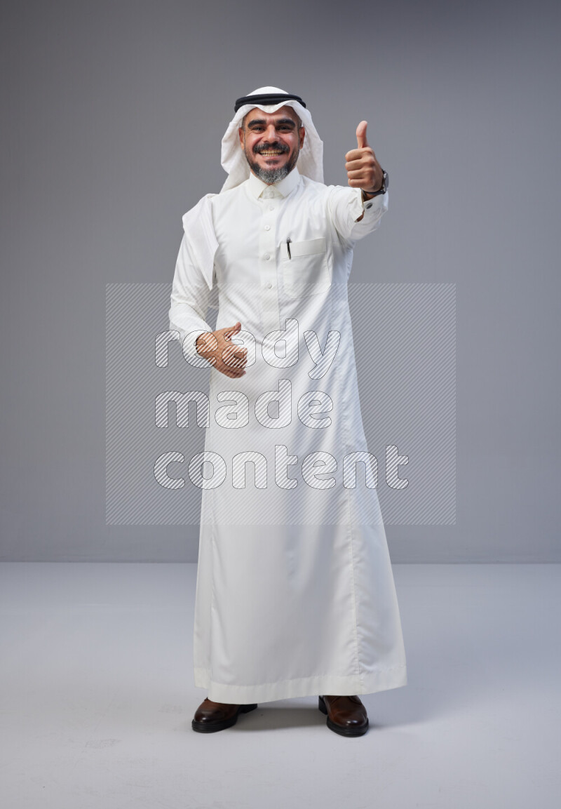 Saudi man Wearing Thob and white Shomag standing interacting with the camera on Gray background