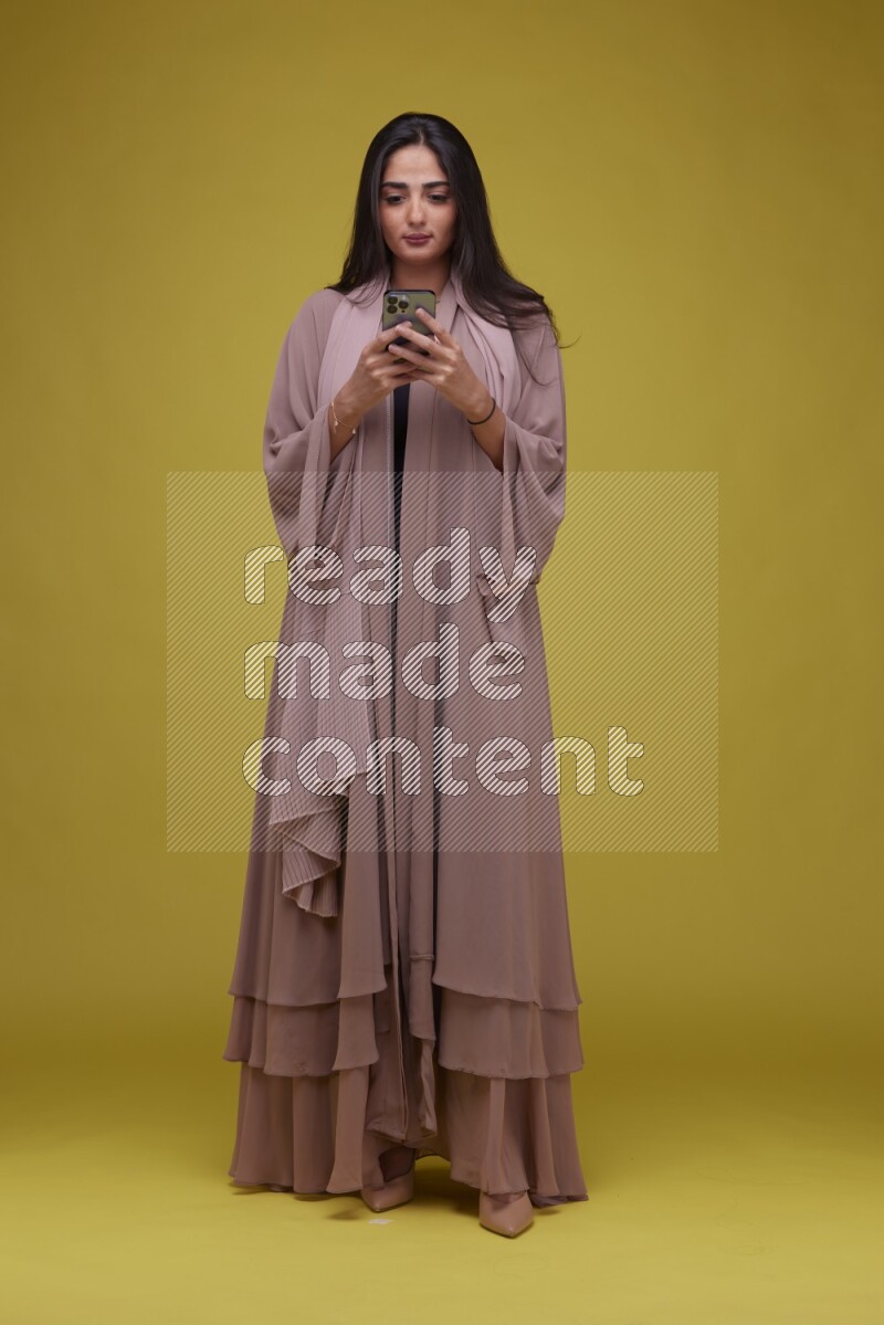 A woman Texting on a Yellow Background wearing Brown Abaya