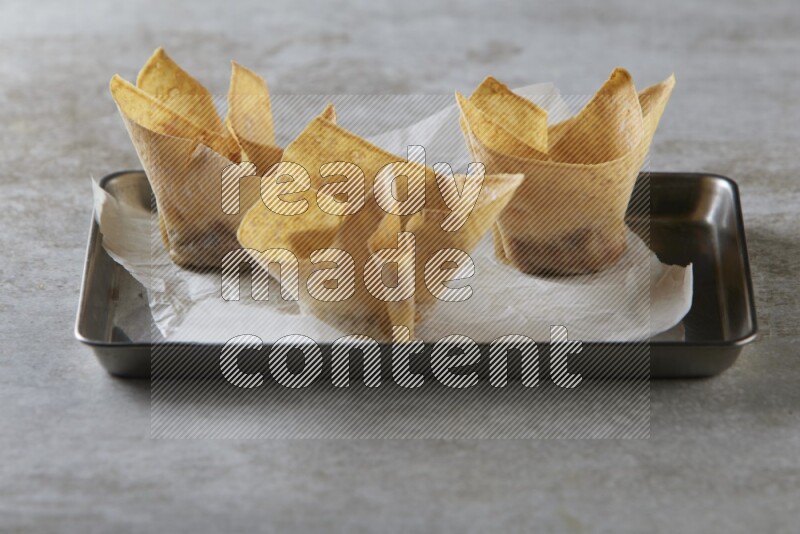 wonton cups on parchment paper in stainless tray on grey textured counter top