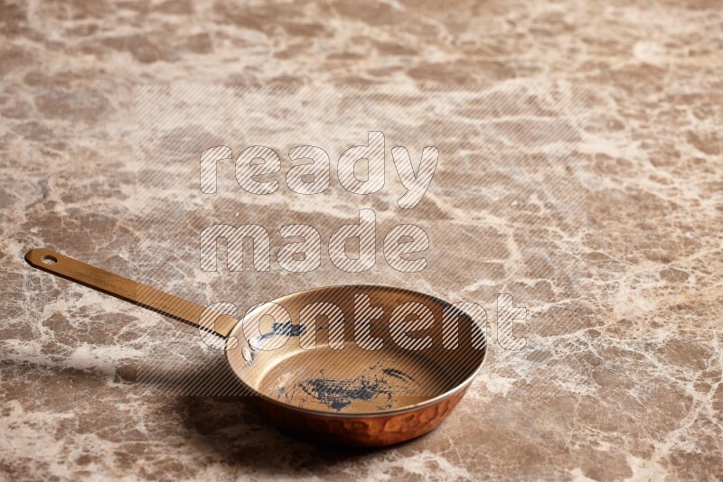 A small copper pan on beige marble background