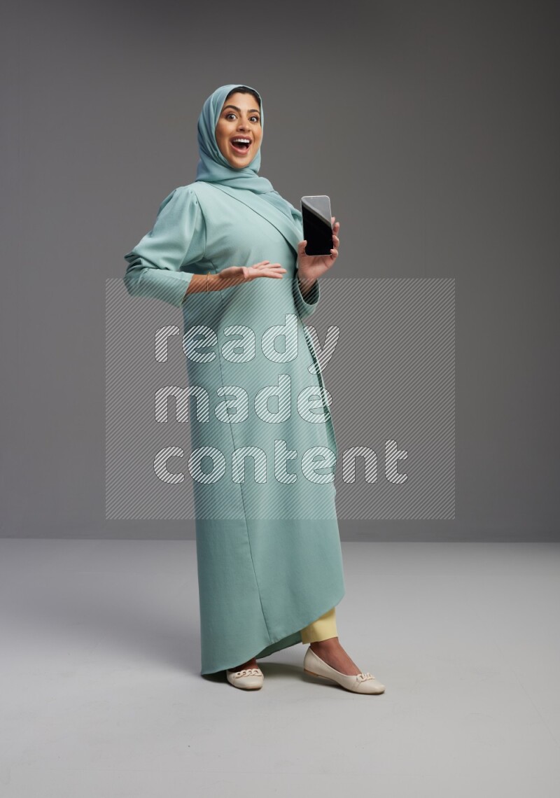 Saudi Woman wearing Abaya standing showing phone to camera on Gray background