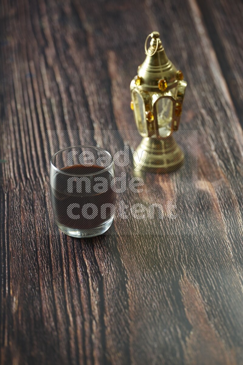 فانوس ذهبي مع مشروبات مختلفة وتمر ومكسرات وسبحة صلاة وقرآن على خلفية خشبية بنية