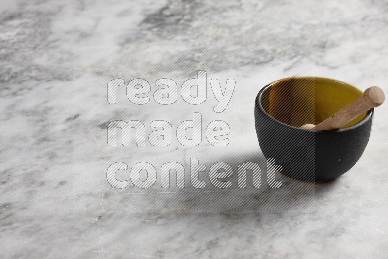 Multicolored pottery bowl with wooden honey dipper in it on grey marble background