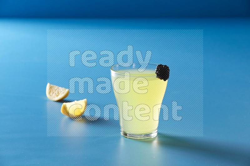 glass of lemon juice with berry on blue background