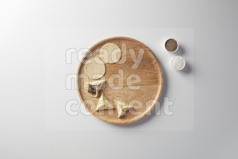 two closed sambosas and one open sambosa filled with meat while salt and black pepper aside in a wooden dish on a white background