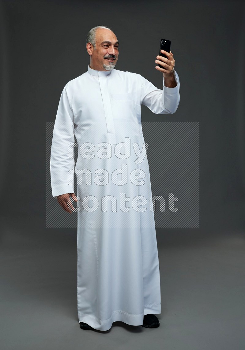 Saudi man without shomag Standing taking selfie on gray background