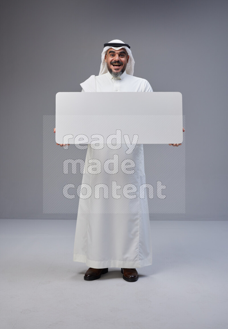Saudi man Wearing Thob and white Shomag standing holding board on Gray background