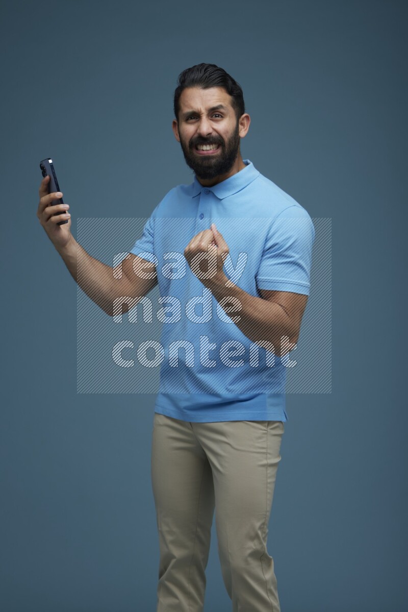 Man posing with a phone in a blue background wearing a Blue shirt