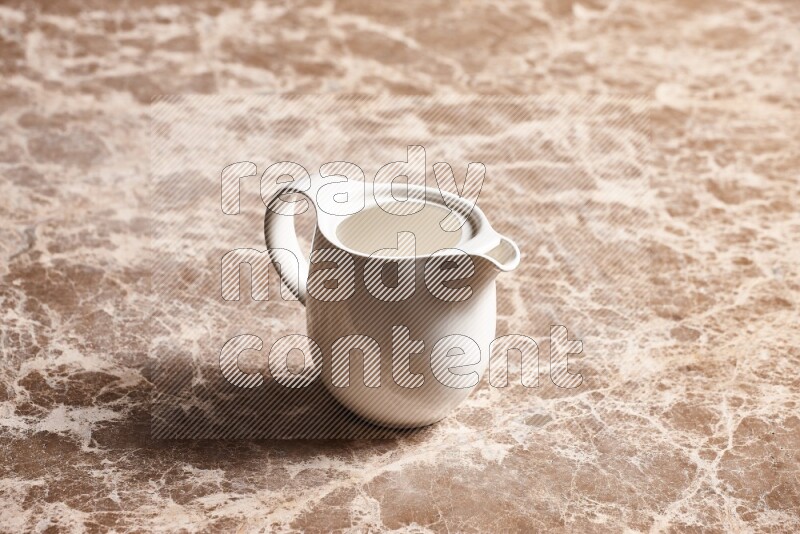 A ceramic milk jug on beige marble background