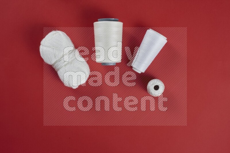 A white collection of sewing and tailoring tools arranged on a red background