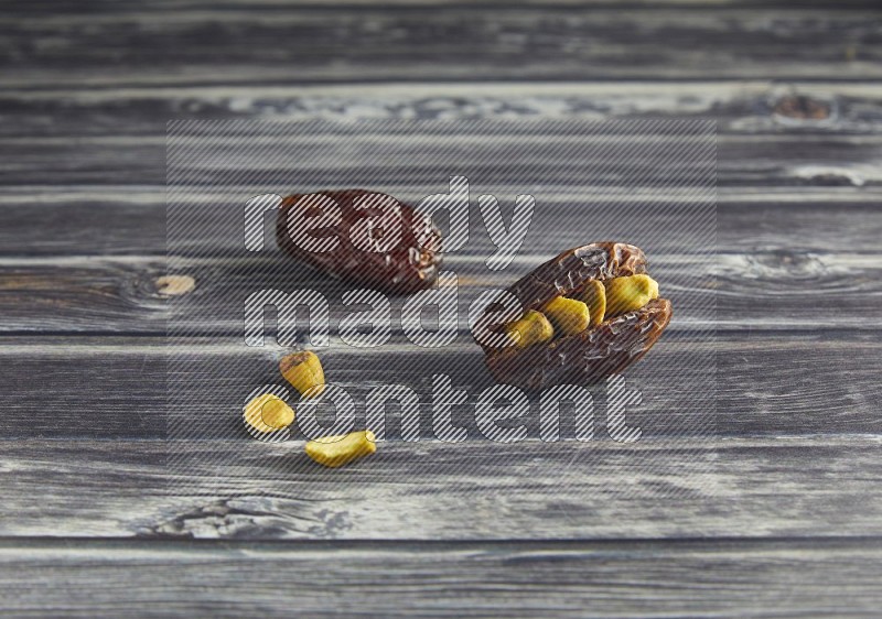 two pistachio stuffed madjoul dates on a wooden grey background