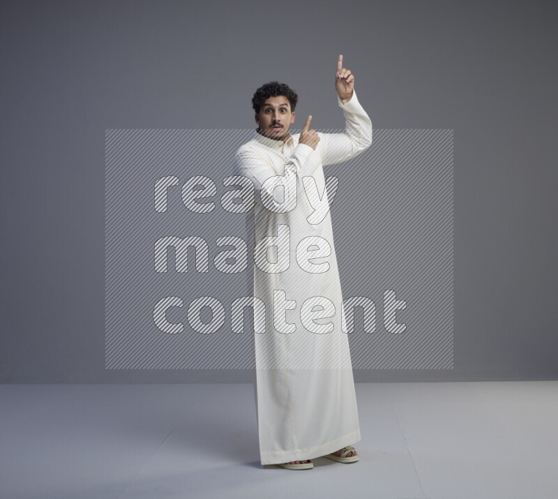 A Saudi man standing wearing thob interacting with the camera on gray background