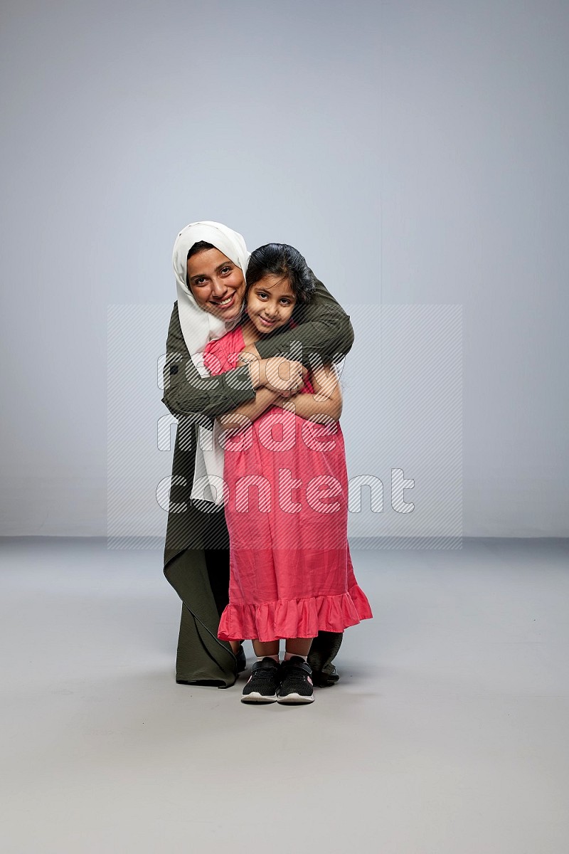 A girl and her mother interacting with the camera on gray background