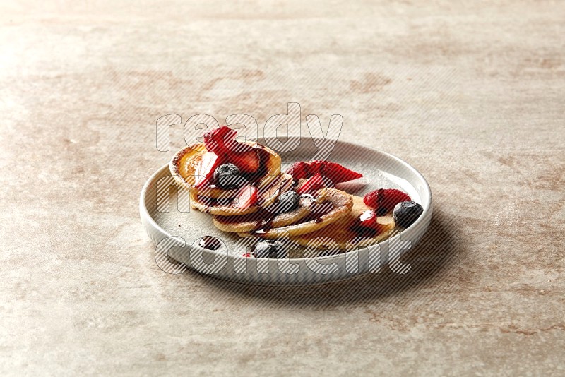 Five stacked mixed berries mini pancakes in a blue plate on beige background