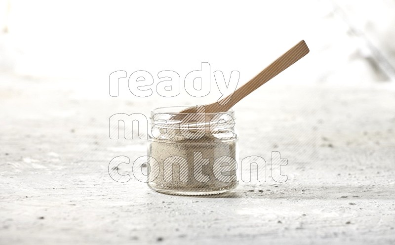 A glass jar and wooden spoon full of white pepper powder on textured white flooring