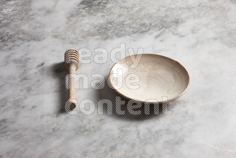 Beige pottery plate with wooden honey dipper on the side on grey marble background