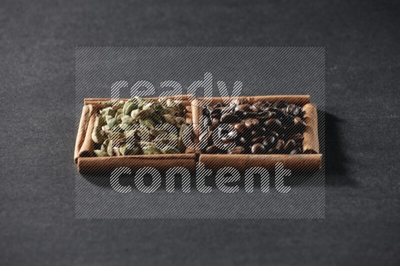 مربعان من أعواد القرفة ممتلئان بحبوب القهوة وحبوب الهيل علي خلفية سوداء