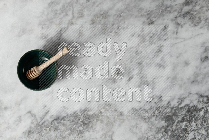 Dark green pottery bowl with wooden honey dipper in it on grey marble background