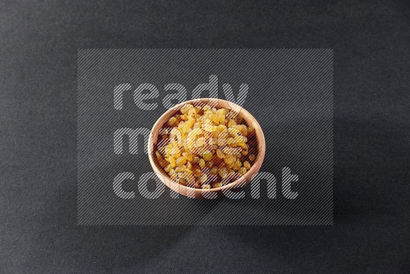 A wooden bowl full of raisins on a black background in different angles