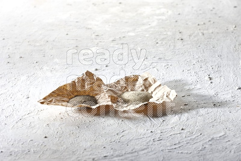 2 Crumpled pieces of paper full of black and white pepper powder on a textured white flooring