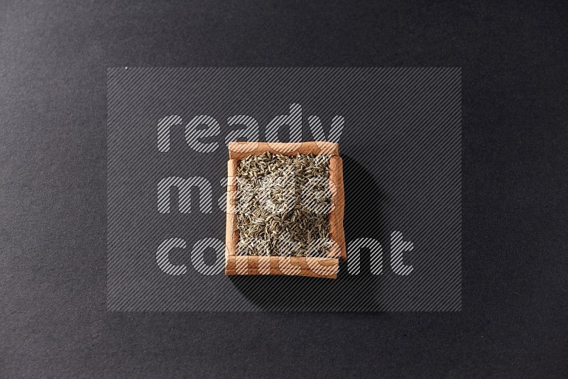 A single square of cinnamon sticks full of cumin on black flooring