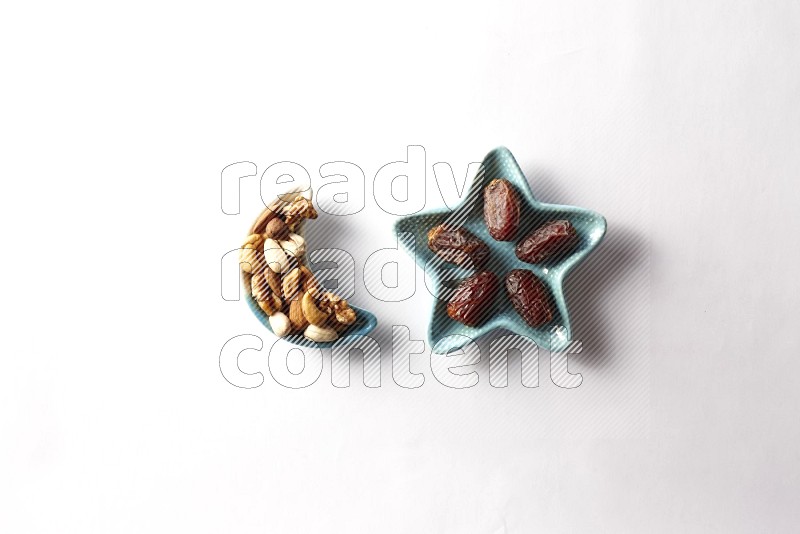 Dates in a star shaped pottery plate and a crescent plate with mixed nuts on white background