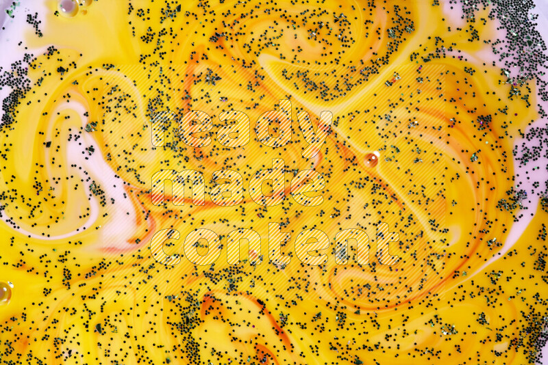 A close-up of sparkling green glitter scattered on swirling yellow, red and pink background