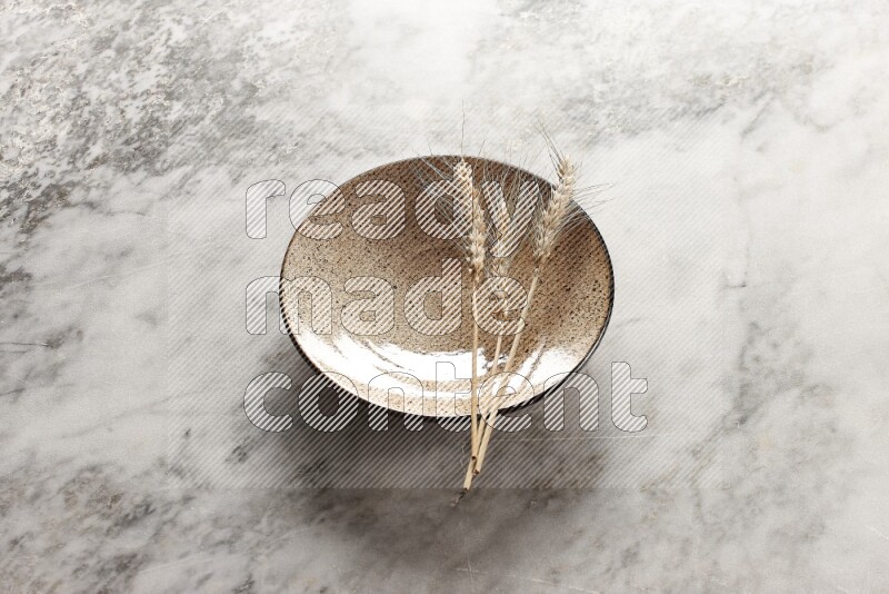 Wheat stalks on multicolored pottery plate on grey marble background