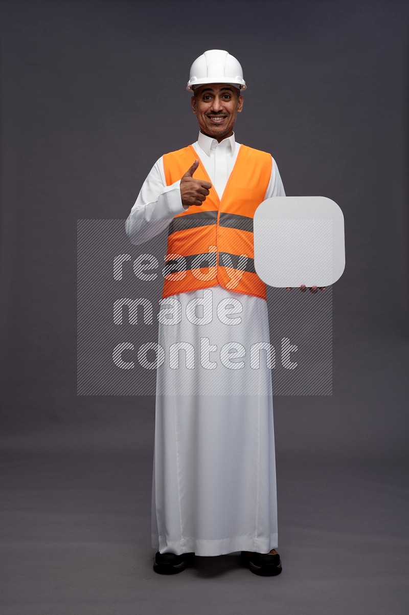 Saudi man wearing thob with engineer vest standing holding social media sign on gray background