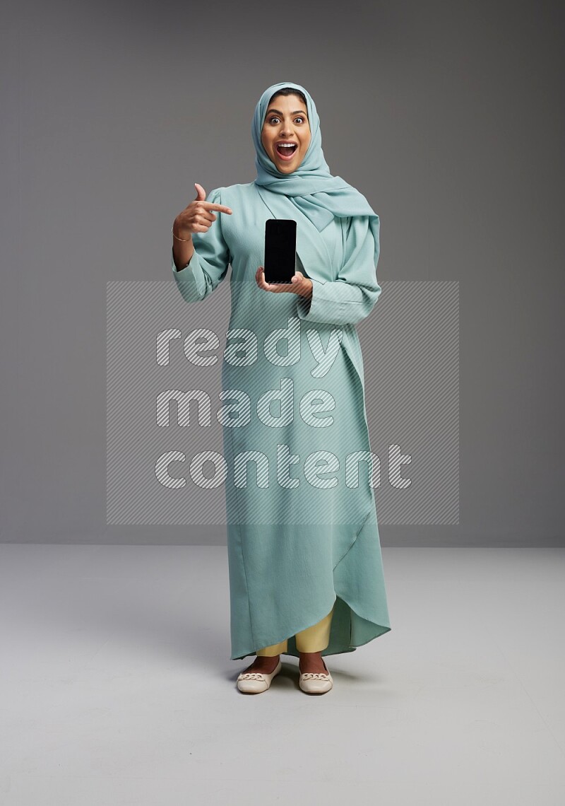 Saudi Woman wearing Abaya standing showing phone to camera on Gray background