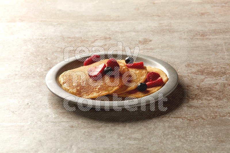 Three stacked mixed berries pancakes in a grey plate on beige background