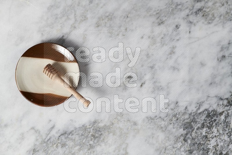 Multicolored Pottery Plate with wooden honey handle in it, on grey marble flooring, Top View