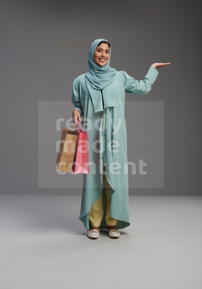 Saudi Woman wearing Abaya standing holding shopping bag on Gray background