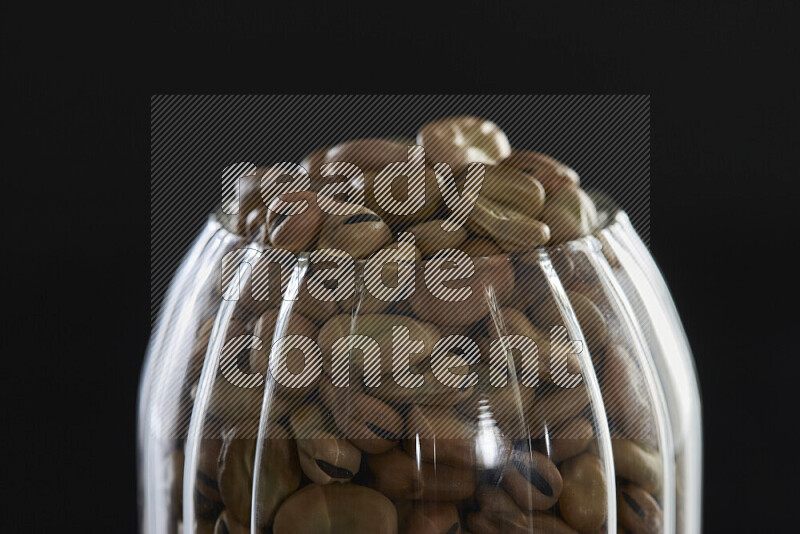 Fava beans in a glass jar on black background