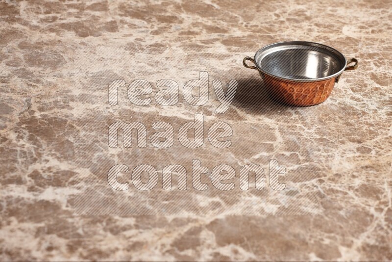 A small copper pot on beige marble background