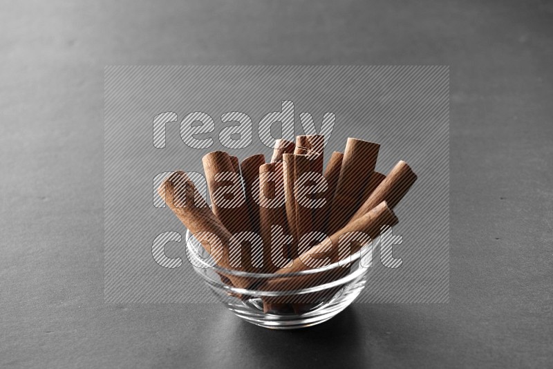 A glass bowl full of cinnamon sticks on black flooring