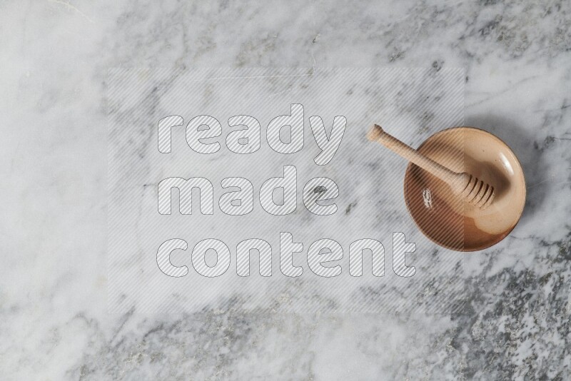 Multicolored pottery plate with wooden honey dipper in it on grey marble background