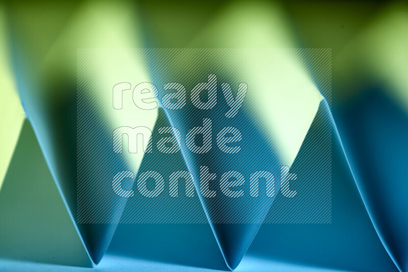 A close-up abstract image showing sharp geometric paper folds in green and blue gradients