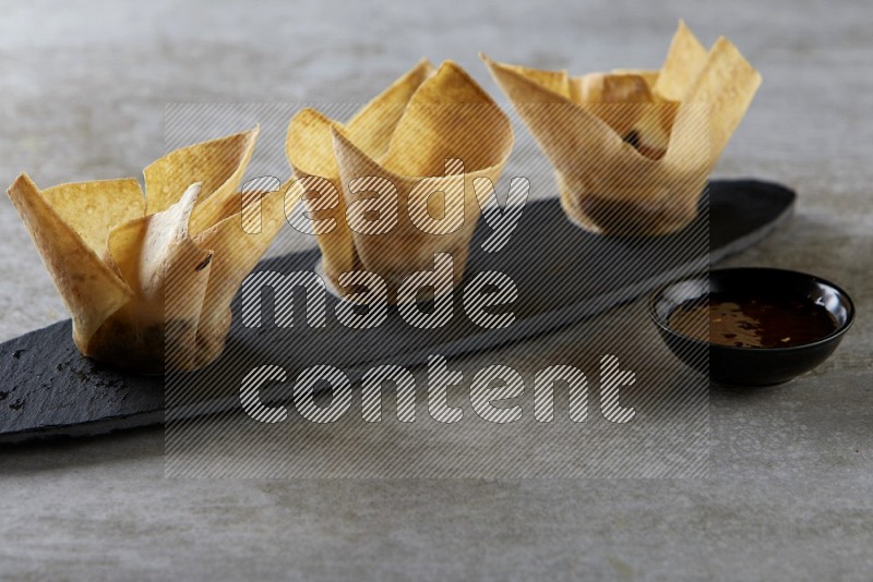 wonton cups with soy sauce ramkin on oval slate on grey textured counter top