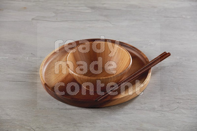brown wood round bowl on top of brown wood round plate and wood chopsticks, on grey textured countertop