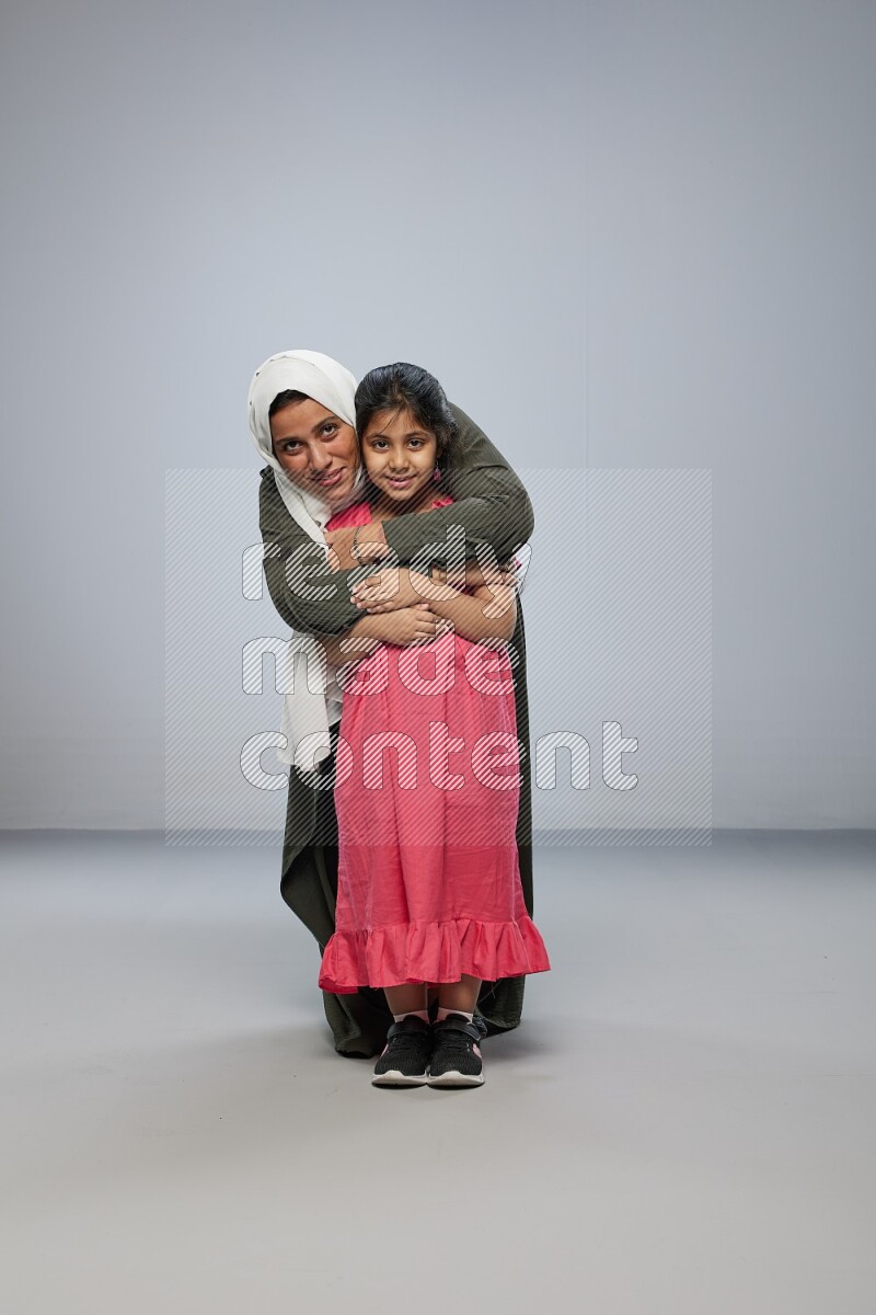 A girl and her mother interacting with the camera on gray background