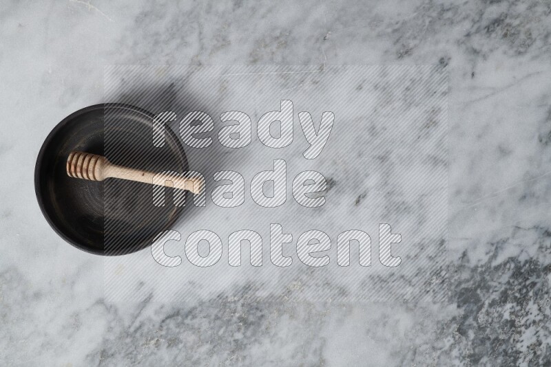 Black pottery oven plate with wooden honey dipper in it on grey marble background