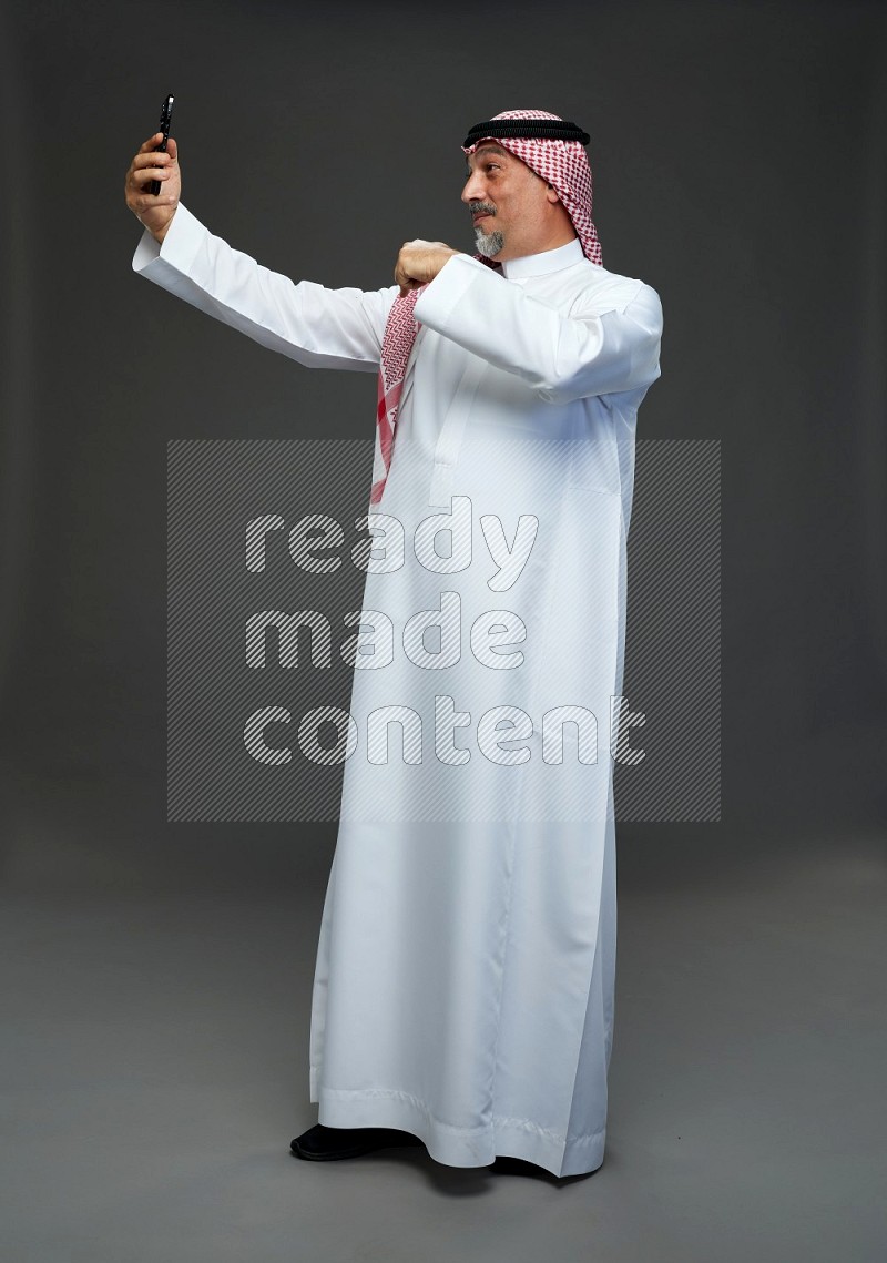 Saudi man with shomag Standing taking selfie on gray background