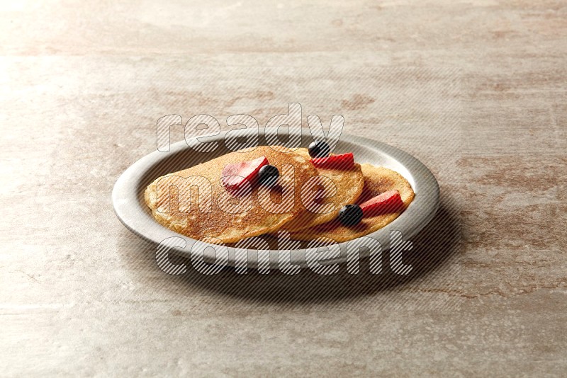 Three stacked mixed berries pancakes in a grey plate on beige background