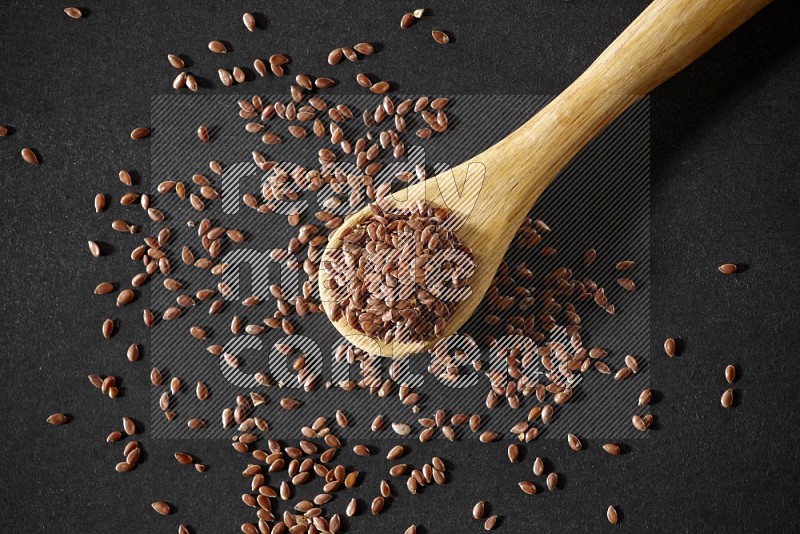 A wooden spoon full of flax and seeds spreaded beside it on a black flooring in different angles